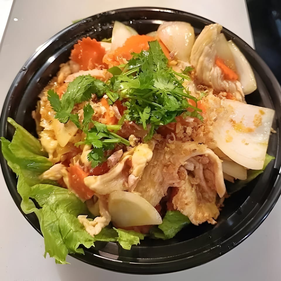 Thai Wok ToGo's chicken dish with onions, carrots, and cilantro in a black bowl.