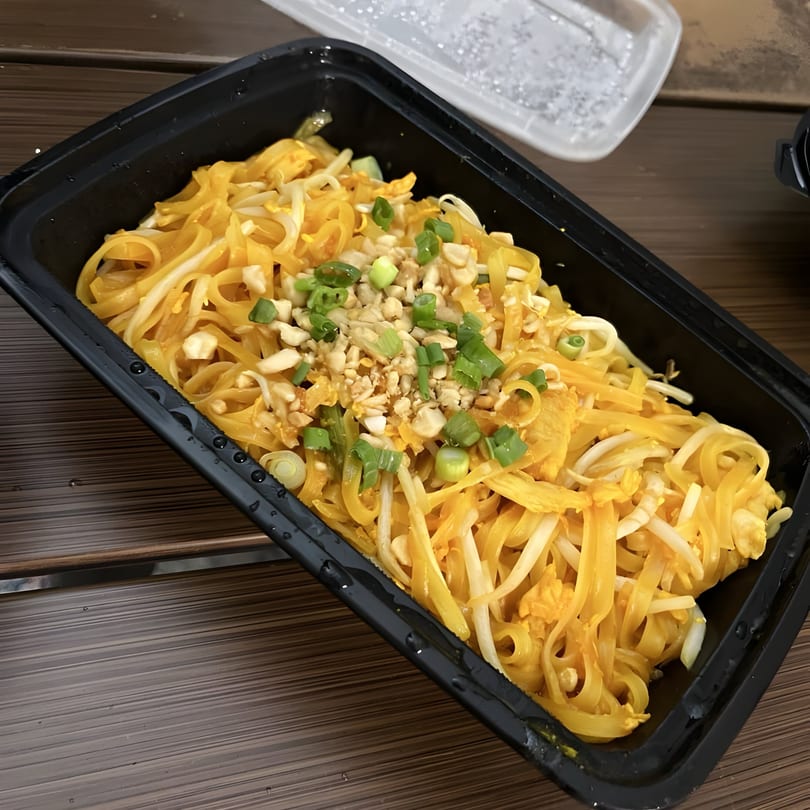 Thai Wok ToGo's Pad Thai noodles with bean sprouts, crushed peanuts, and green onions in a black container.