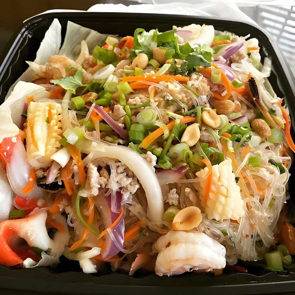 Close-up of a Thai glass noodle salad with shrimp, squid, vegetables, and peanuts in a black container.