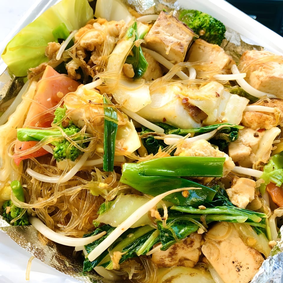 Close-up of Thai Wok ToGo's glass noodles with tofu, broccoli, cabbage, and green onions in a foil container.