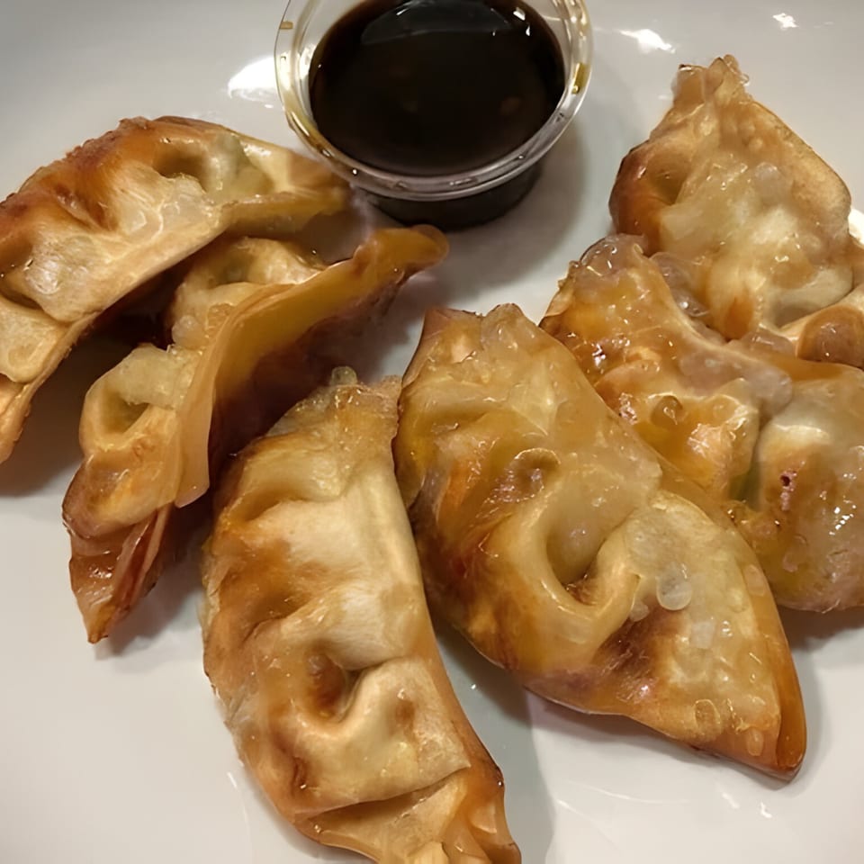 Golden-brown Thai dumplings, glistening with sauce, arranged on a white plate with a small cup of dipping sauce.
